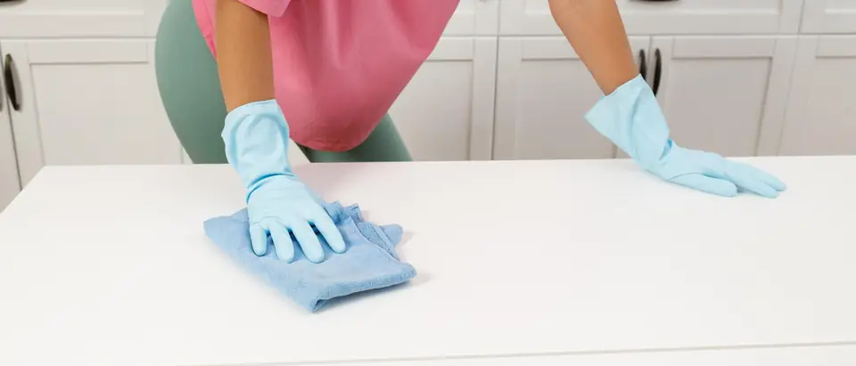 A person in pale blue rubber gloves wiping a white kitchen counter with a blue cloth